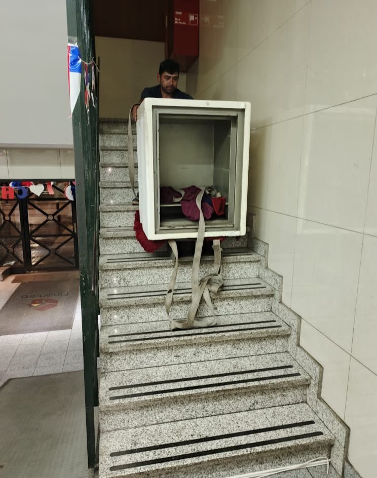 Técnico bajando una caja fuerte blanca por una escalera de granito con eslingas, en edificio de oficinas del centro de Santiago