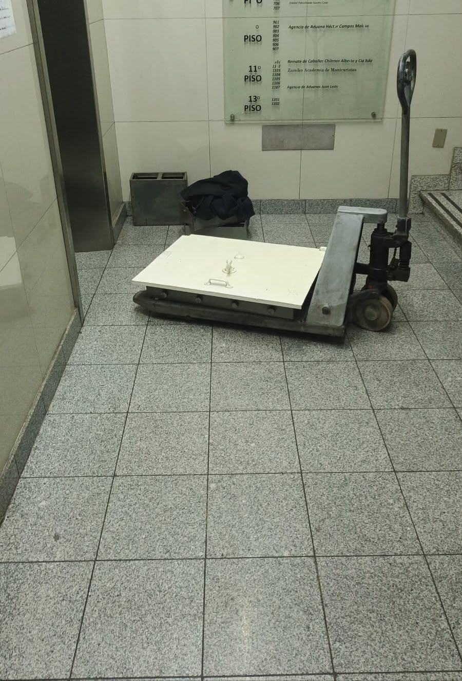 Caja fuerte blanca acostada sobre transpaleta en el hall de un edificio de oficinas, junto al ascensor